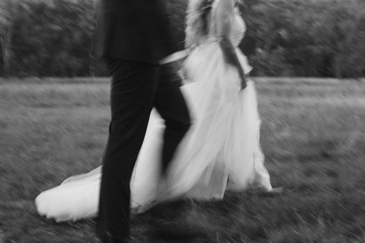 Black and white editorial wedding image of a couple walking through grass